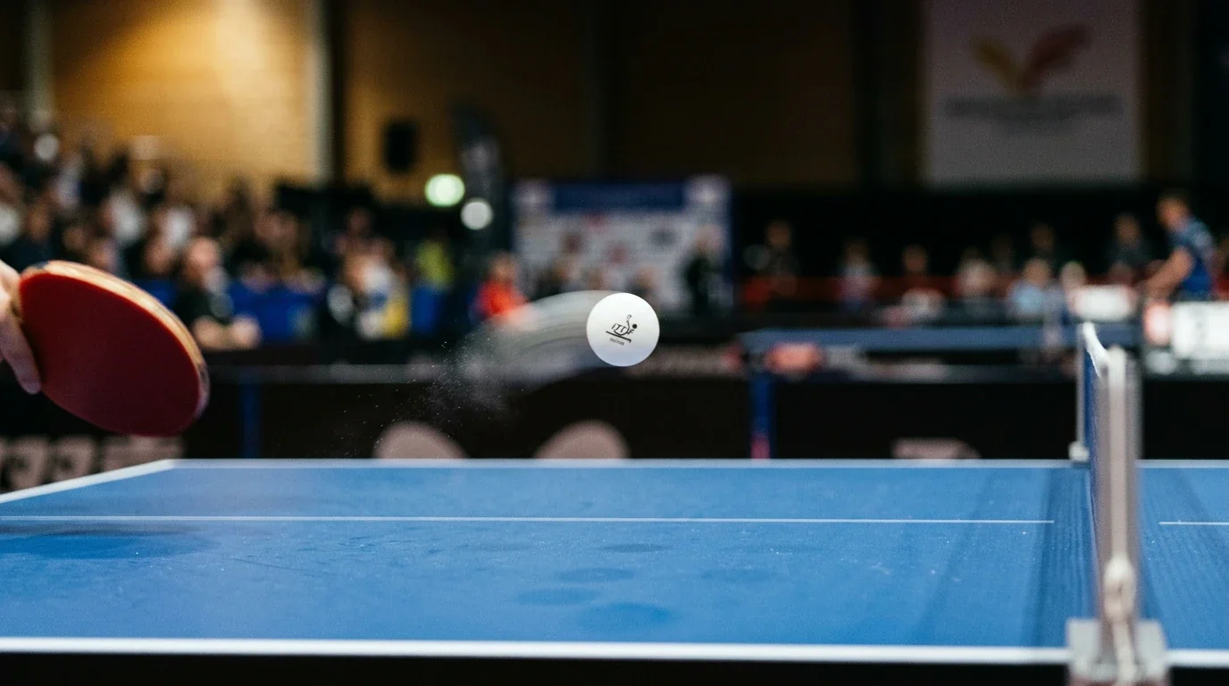 Detalle de pelota de tenis de mesa en vuelo con rastro de topspin sobre mesa azul